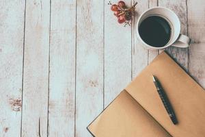 Top view of Coffee cup with blank notebook,pen and grape on white wooden table background, Vintage tone, Free space for text photo