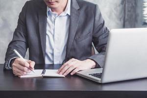 Close up of Businessman writing some data in notebook and working on laptop at the office. photo