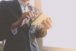 Close up of businessman using tablet device while standing at a window in an office photo