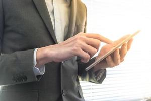 Close up of businessman using tablet device while standing at a window in an office