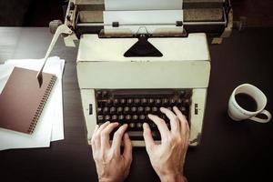 primer plano de manos masculinas escribiendo en máquina de escribir en el escritorio. tono antiguo foto