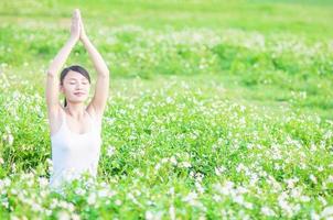 jovencita haciendo ejercicio de yoga en un campo verde con pequeñas flores blancas en el área al aire libre que muestra calma y paz en la mente de meditación - la gente practica yoga para la meditación y el concepto de ejercicio foto