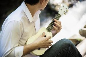 Man play ukulele new to the river- people and music instrument life style in nature concept