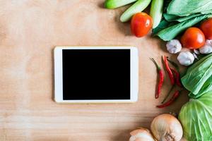 Top view of Fresh vegetables with tablet touch computer gadget on wooden table background. photo