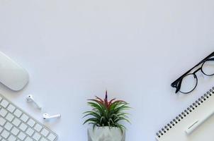 fondo del concepto de espacio de trabajo con planta de aire tillandsia, ratón, teclado, auricular, portátil, bolígrafo y gafas sobre fondo blanco. foto