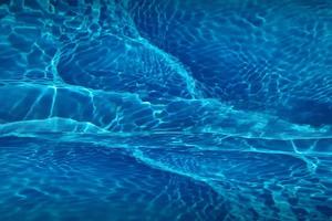 Defocus blurred blue water shining in the swimming pool. rippled water detail background. The water surface in the sea, ocean background. Water wave under sea texture background.