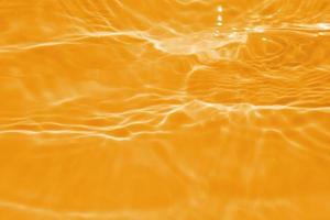 Defocus blurred transparent orange colored clear calm water surface texture with splashes and bubble. Trendy abstract nature background. Water wave in sunlight with copy space. Blue watercolor texture photo