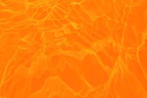 desenfoque borroso transparente color naranja claro agua tranquila textura superficial con salpicaduras y burbujas. fondo de naturaleza abstracta de moda. onda de agua a la luz del sol con espacio de copia. textura de acuarela azul foto