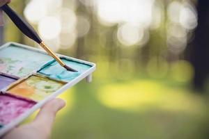 Relax woman painting water colour art work in green garden forest nature - people with creative art in nature stress reduction and meditation concept photo