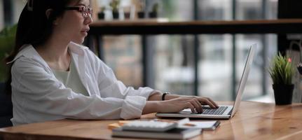 Beautiful young asian woman sitting at coffee shop using laptop. Happy young businesswoman sitting at table in cafe with tab top computer. photo