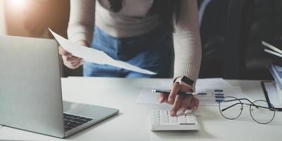 concepto de finanzas la mujer sostiene un bolígrafo gráfico, presiona una calculadora y gana dinero escribiendo informes y memorandos, y analizando documentos comerciales con una computadora portátil verticalmente. foto