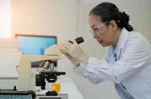 científica del laboratorio de desarrollo médico que mira bajo el microscopio, analiza la muestra de la placa de petri. en el fondo un gran laboratorio farmacéutico con especialistas en medicina foto