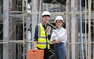 dos ingenieros, arquitectos o capataces confiados de pie con los brazos cruzados posan frente al sitio de construcción como fondo. foto