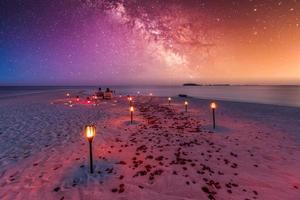 Destination dining, honeymoon, anniversary. Amazing romantic dinner beach on wooden deck with candles under sunset sky. Romance and love, luxury destination dinning, exotic table setup with sea view