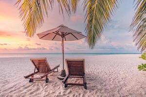 Beautiful tropical sunset scenery, two sun beds, loungers, umbrella under palm tree. White sand, sea view with horizon, colorful twilight sky, calmness and relaxation. Inspirational beach resort hotel photo