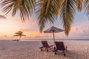 Beautiful tropical sunset scenery, two sun beds, loungers, umbrella under palm tree. White sand, sea view with horizon, colorful twilight sky, calmness and relaxation. Inspirational beach resort hotel photo