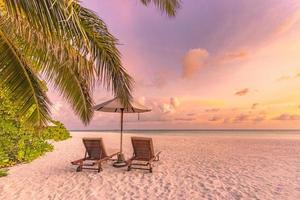 Beautiful tropical sunset scenery, two sun beds, loungers, umbrella under palm tree. White sand, sea view with horizon, colorful twilight sky, calmness and relaxation. Inspirational beach resort hotel photo