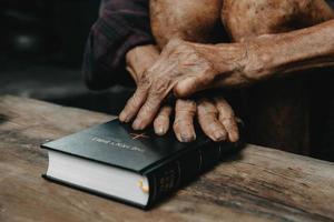 manos juntas en oración a dios junto con la biblia en el concepto cristiano y la religión, el anciano ora en la biblia foto