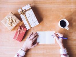 Top view of Male writing some data in card, Gift boxes and coffee cup on wooden table. photo