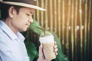 hombre asiático casual bebe café helado felizmente en la naturaleza - gente con café en el concepto de naturaleza foto