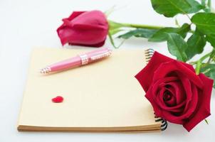 rosa roja y bolígrafo rosa con cuaderno sobre fondo blanco - concepto de tarjeta electrónica de amor y flor foto