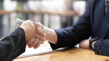 An Asian female lawyer or business legal consultant at the office desk receives money and shaking hand with her male client. cropped image photo