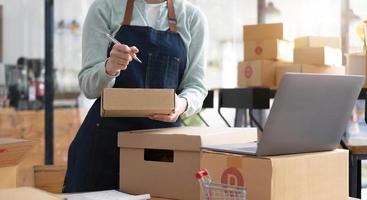 Startup Entrepreneurship Small Business SME Freelance Young lady working at home with boxes and laptop online Marketing Packaging SME Shipping Ecommerce Concepts photo