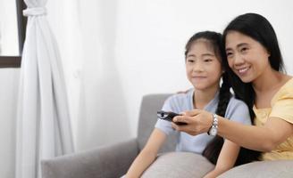 Happy asian parents sit on comfortable couch in living room with little kids watch TV enjoy home weekend enjoying movie photo