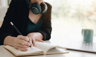 retrato de una mujer asiática bastante joven que estudia en línea con una computadora portátil mientras se sienta en la mesa y el cuaderno en casa. foto