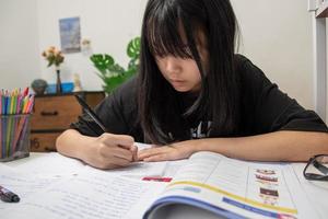 una estudiante asiática está escribiendo deberes y leyendo un libro en el escritorio foto