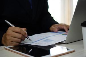 businessman holding pen to work computer graphs and charts data statistical data financial analysis documents. photo