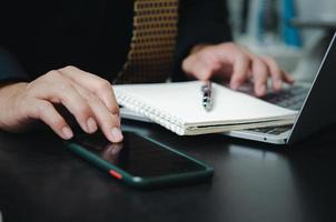 Businessman touching mobile smart phone digital internet technology network with computer laptop and pen book on desk. photo