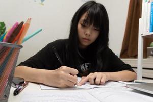 una estudiante asiática está escribiendo deberes y leyendo un libro en el escritorio foto