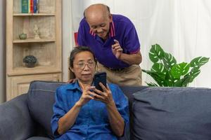 Asian senior holding mobile smart phone communication online internet video call together on sofa at home. photo