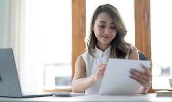 Beautiful young asian woman sitting at coffee shop using laptop. Happy young businesswoman sitting at table in cafe with tab top computer. photo