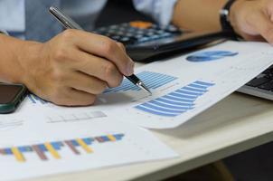 businessman holding pen to work computer graphs and charts data statistical data financial analysis documents. photo