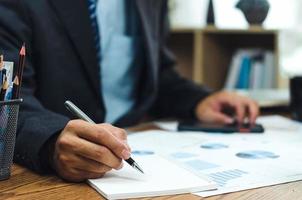 hombre de negocios sosteniendo un bolígrafo escribiendo un libro y un documento gráfico contabilidad finanzas papel trabajo análisis gráfico marketing inversión e informe economía en el escritorio de la oficina. foto