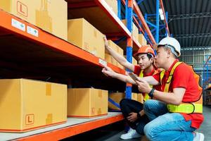 Asian male worker talking with manager in warehouse store. man engineers people wear safety hard helmet and vest checking storage box parcel in factory. Bangkok Thailand photo