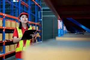 Portrait of smiling asian manager worker woman standing and order details on clipboard document for checking goods and supplies on shelves with goods background in warehouse. photo