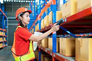 Female worker with protective vest and scanner, holds document, standing at warehouse of freight forwarding company, scanning qr code for delivery photo