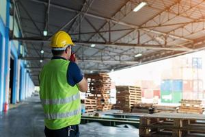 the caucasian engineer using walky talky comunicate with lifting container team with blue sky. Logistics transportation industry forklift handling container box loading stacker. back side worker view. photo