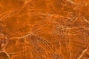 desenfoque de agua naranja borrosa que brilla en el mar. fondo de detalle de agua ondulada. la superficie del agua en el mar, fondo del océano. ola de agua bajo el fondo de la textura del mar. foto