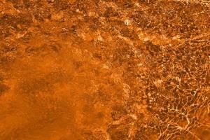 desenfoque de agua naranja borrosa que brilla en el mar. fondo de detalle de agua ondulada. la superficie del agua en el mar, fondo del océano. ola de agua bajo el fondo de la textura del mar. foto