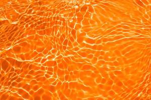 Defocus blurred transparent orange colored clear calm water surface texture with splashes and bubble. Trendy abstract nature background. Water wave in sunlight with copy space. Blue watercolor texture photo