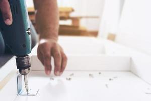 el hombre está trabajando con el montaje de muebles usando un destornillador eléctrico en la instalación de una nueva casa - trabajo técnico en el lugar usando el concepto de herramientas manuales foto