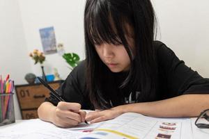 una estudiante asiática está escribiendo deberes y leyendo un libro en el escritorio foto