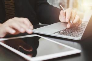 Businessman holding pen typing keyboard computer laptop and tablet on desk. Business technology digital internet work job research and communication concept. photo