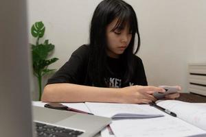 una estudiante asiática está escribiendo deberes y leyendo un libro en el escritorio foto