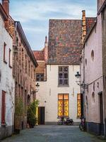 The front view of a beautiful house with its cute roof made of red and black bricks on a narrow street in Bruges, Belgium. photo