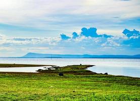 lake scenery  There is a mound covered with green grass.  A distant mountain near the horizon where black rain clouds were forming in the  day with inclement weather photo